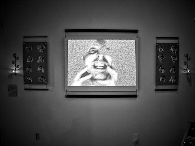 Static Insanity | Gallery Photo — This setup I really, really enjoyed. It's not perfect, but it is so close to perfect. As you can see, the video doesn't actually go all the way to the edges of the suspended blank frame, but it's kind of whatever. These ones are suspended by chains, but in a vertical format, kind of reminding me of some Japanese artwork look, but still using a crossbar and chains with candles at each end. This part of the gallery was kept dark so that the shitty projector could actually project a decent image.