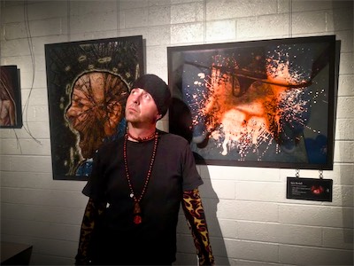 Cult of Ego II | Gallery Photo | Burnt Sky — At this show, I was invited by a friend who was putting on a show at Burnt Sky Studios. This was right in the Arts District, about a block south of Roosevelt Row in Phoenix, Arizona. And he was looking to fill up a gallery space with a group show, and, well, I had a few pieces printed and picked some out and joined up. What we see here is me, I don't know what I was doing. It's not exactly an unusual look for me, but it's also something I maybe wore once in that particular combination. I don't usually wear sleeves or whatever that necklace is. And I was doing what I could to feel confident in a time of extreme loss.